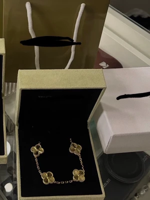 Guldigt armband med fyrklöver - Exklusivt armband med fem  fyrklöver i guldton. Kedjan är tunn och elegant, och varje klöver har detaljerade kanter som ger en lyxig känsla. Perfekt för dig som gillar klassiska och tidlösa smycken.