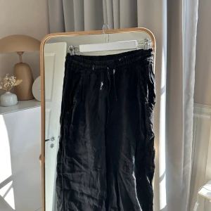 Svarta linnebyxor med resårmidja - Säljer ett par svarta linnebyxor med avslappnad passform och resår i midjan. Byxorna har raka ben och är tillverkade i ett luftigt linnematerial, perfekta för en chill och stilren look.