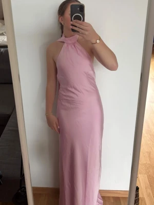 Ljusrosa långklänning med knyt - Säljer en elegant ljusrosa långklänning med halterneck och knyt i ryggen. Klänningen har öppen rygg och är tillverkad i ett mjukt, glansigt material som ger en lyxig känsla. Perfekt för speciella tillfällen så som bal, bröllop eller middagar💕