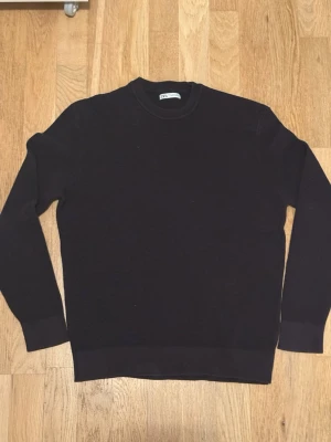 Svart stickad tröja från Zara Man - En stilren svart stickad tröja från Zara Man med rund halsringning och långa ärmar. Tröjan har en enkel, klassisk design och ribbade muddar vid ärmslut och nederkant. Perfekt att matcha med jeans eller chinos.