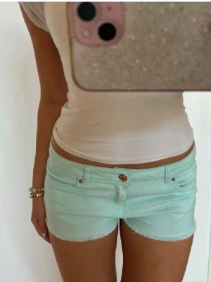 Mintgröna denimshorts med rå kant - Säljer ett par mintgröna shorts i denim med rå kant nertill och klassisk femficksdesign. Midjemått- 42