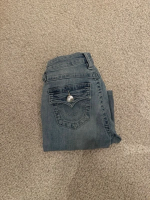 Blå bootcut jeans från True Religion - Säljer ett par ljus blå true religion jeans i modellen Becca, inte för hög midjade utan mid waist. Med silver knappar. Super fina och man ser inga tydliga tecken på användning💕💞