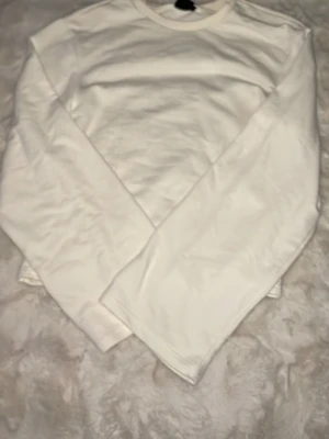 Vit basic långärmad tröja - En enkel vit långärmad tröja med rund halsringning. Tröjan har en rak passform och är tillverkad i ett mjukt material som passar perfekt till lager på lager. Stilren och lätt att matcha med olika outfits. Storlek XS . Använd 1 gång . Pris 40kr