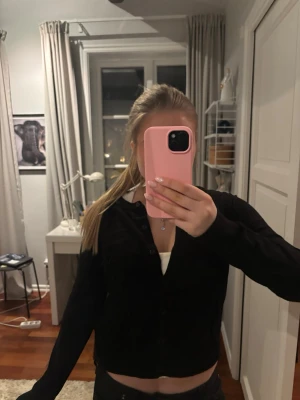 Svart cardigan med v-ringning - Svart, långärmad cardigan med v-ringning och knäppning framtill. Enkel och stilren design som passar till många olika outfits. Tröjan har en något croppad passform och är tillverkad i ett mjukt material.