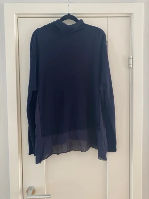 Mörkblå polotröja med transparent nederdel - Snygg mörkblå polotröja med lång ärm och transparent nederdel. Tröjan har en lös passform och är tillverkad i ett tunt, lätt material som ger en cool layering-effekt. Perfekt för dig som gillar stilrena plagg med en twist. Atos Lombardini marinblå polotröja strl 44 ull och viskos  Endast använd vid ett par tillfällen och är i fint begagnat skick  Mått Över bröstet: ca 73 cm Längd från axeln och ner: ca 69 cm  Ull och viskos  Kommer från ett djur och rökfritt hem 
