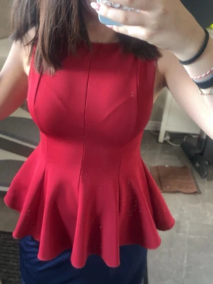 Röd peplum topp med volang - Snygg röd peplum topp med breda axelband och volang nedtill. Toppen har en figurnära passform upptill och markerad midja som ger en feminin siluett. Perfekt att styla med jeans eller kjol för en trendig look.