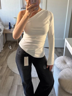 Vit oneshoulder topp - Snygg vit oneshoulder topp med lång ärm på ena sidan och axelbandslös på andra. Toppens passform är slim och materialet känns mjukt, troligtvis bomull eller polyester. Perfekt för dig som vill ha en clean och modern look.