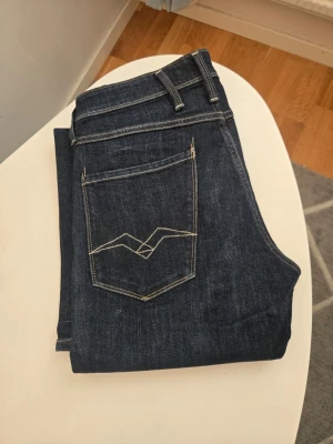 Mörkblå jeans från Replay w31 L32 - Snygga mörkblå jeans från Replay med klassisk femficksdesign och kontrastsömmar. Jeansen har raka ben och tydliga detaljer på bakfickan. Perfekta för dig som gillar stilrena och tidlösa jeans i denim.