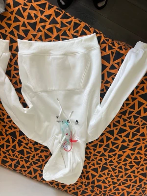 Vit hoodie från Off-White - Säljer en clean vit hoodie från Off-White med svart tryck på bröstet och klassiska Off-White detaljer. Hoodien har dragsko i huvan och stor magficka framtill. Perfekt för dig som gillar streetwear och vill ha något stilrent men ändå unikt.