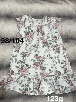 Blommigt volangnattlinne - Supersöt nattlinne med blommigt mönster i rosa och grönt. Nattlinnet har volangkant nertill och korta ärmar, perfekt för varma nätter. Bekväm passform och romantisk stil.🌸 Fint använt skick. Storlek 98/104