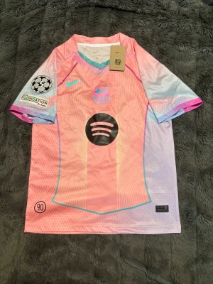Barça 25/26 tröja med Lamine Yamal - Säljer en Barcelona matchtröja i rosa och ljusblå toner med tryck 'Lamine Yamal 10' på ryggen. Tröjan har Champions League-märke på ärmen, Spotify-logga på bröstet och klubbmärke framtill. Tillverkad i lätt, ventilerande material och har korta ärmar. Priset är inte hugget i sten men jag kommer inte acceptera löjliga offer!