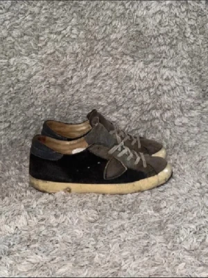 Svarta och gråa sneakers i mocka - Säljer ett par svarta och gråa sneakers med ovandel i mocka och textil. Skorna har grå snörning och en vit, något sliten sula. Klassisk låg modell med enkel design som passar till många olika stilar. Sulan är i dåligt skick på båda skorna men går att repareras. skriv gärna vid frågor! ☺️