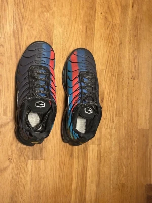 Nike Air Max Plus blå/röd sneakers - Nike Air Max Plus sneakers med en grym färgskiftning från blått till rött och svarta detaljer. Skorna har synlig Air-dämpning i sulan, svarta snören och mesh-överdel med vågiga svarta linjer. Swoosh-logga på sidan och robust yttersula.