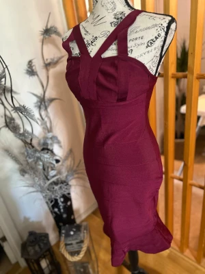 Vinröd tight kort klänning - Snygg vinröd bandage klänning med breda axelband och figurnära passform. Klänningen har en modern design med markerade sömmar och är ärmlös. Perfekt för dig som vill sticka ut med en elegant och trendig look.