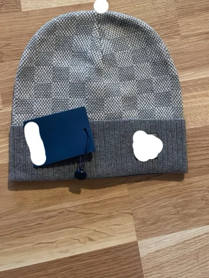 Gråmelerad ribbad mössa - Snygg gråmelerad mössa med diskret rutmönster och uppvikt kant i ribbstickning. Perfekt accessoar för kyliga dagar och passar till de flesta stilar. Mössan har en modern, avslappnad passform och är tillverkad i mjukt material.