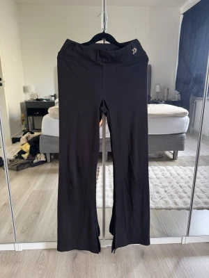 Svarta utsvängda leggings med slits - Säljer ett par svarta leggings med utsvängda ben och slits framtill. De har hög midja och är tillverkade i ett stretchigt material som sitter bekvämt. Perfekta för dig som gillar en trendig och stilren look.