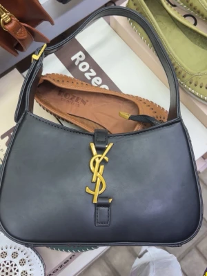 Svart axelväska med guldlogo - Stilren svart handväska i slät läderlook med  ger en lyxig känsla. Perfekt för dig som gillar klassiska accessoarer med statement-detaljer.