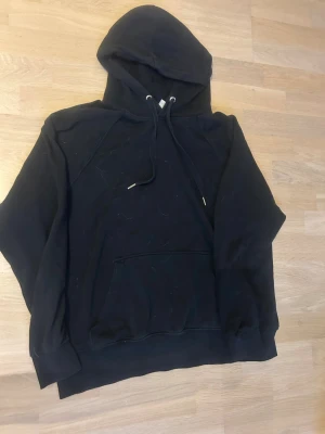 Svart hoodie med magficka och huva - En enkel svart hoodie med klassisk huva och dragsnören. Hoodien har en stor magficka framtill och ribbade muddar vid ärmsluten. Perfekt för en avslappnad och chill stil. 