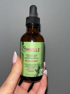 Mielle Rosemary Mint hår- och hårbottenolja - Mielle Rosemary Mint Scalp & Hair Strengthening Oil är en stärkande olja för hår och hårbotten, berikad med biotin. Kommer i en brun glasflaska med pipett och har en grön etikett. Innehåller rosmarin och mynta för en fräsch känsla. Helt oanvänd, utan förpackning 