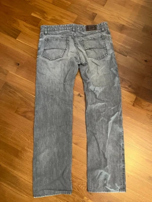 Ljusgrå jeans från Hugo Boss - Säljer ett par ljusgrå jeans från Hugo Boss med klassisk femficksdesign och en snygg detaljsöm på bakfickan. Jeansen har normal passform och är tillverkade i mjukt bomullstyg. Perfekta för dig som gillar en avslappnad men stilren look. I jeansen står det att storleken är W33 L34 men egentligen så är det som ett par W31 L32. Hör av dig om du har några funderingar!