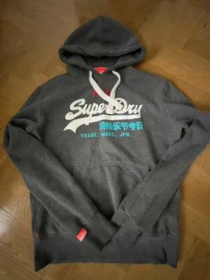 Mörkgrå Superdry hoodie - En fet SuperDry hoodie som kommer ge dig blickar vart du än går. Skitbra för snygga outfits. Hade behållt den men var för stor för mig tyvärr. Kan gå ner i pris vid snabb affär! 