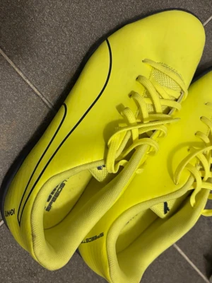 Gula fotbollsskor från Puma - Snygga lime fotbollsskor från Puma med svarta detaljer och klassisk logga på plösen. Skorna har snörning och en smal, sportig siluett. Ovandelen är i syntetmaterial som ger bra bollkontroll och komfort på planen. Är i typ helt ny