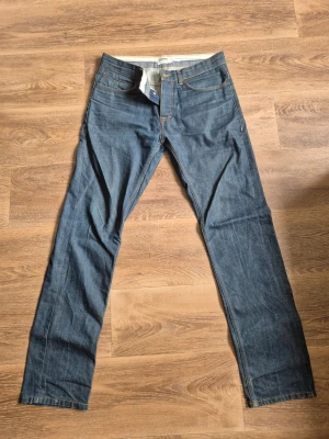 Blå  jeans från Dobber - Säljer ett par klassiska blå jeans från Dobber med raka ben och knappgylf. Jeansen har fem fickor och snygga kontrastsömmar. tillverkade i slitstarkt denimtyg. Inga skavanker!