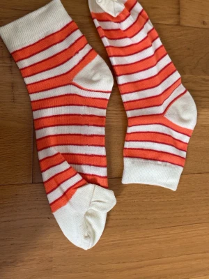 Randiga tåstrumpor i orange och vitt - Säljer ett par tåstrumpor med orange och vita ränder. Strumporna har separata fack för varje tå och är tillverkade i mjuk bomull. Perfekta för dig som vill ha något annorlunda och bekvämt på fötterna.