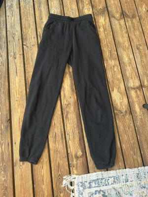 Svarta mjukisbyxor med NYC-brodyr - Säljer ett par svarta mjukisbyxor med broderad NYC-text på ena sidan. Byxorna har resår i midjan och vid bensluten samt två sidofickor. Perfekta för chill dagar eller när du vill ha det bekvämt. Materialet känns mjukt och skönt mot huden.