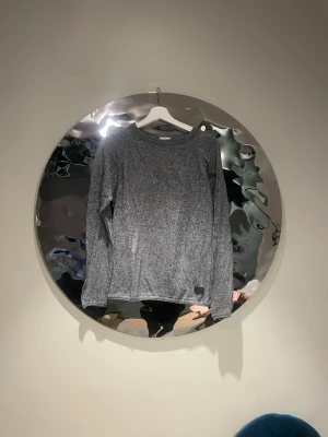 Gråmelerad stickad tröja - En stilren gråmelerad stickad tröja med rund halsringning och långa ärmar. share-etikett syns nedtill på framsidan. Tröjan har en mjuk och bekväm känsla, perfekt för lager på lager och enkel under jackan. Passar till jeans eller kjol för en avslappnad look.