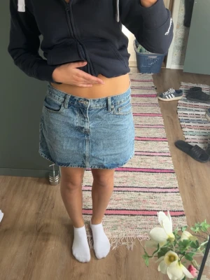 Blå jeanskjol med fickor - Säljer en klassisk blå jeanskjol i kort modell med fram- och bakfickor. Kjolen har en rak passform och stängs med dragkedja och knapp framtill. Perfekt till sommaren och enkel att matcha med olika toppar.