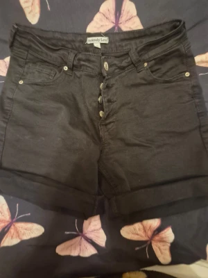 Svarta high waist shorts Sincerely Loved - Svarta shorts från Sincerely Loved med hög midja och knappgylf  lagom långa ben. Klassisk femficksmodell och tillverkade sopig bomullsmix. Perfekta för sommaren och passar till allt.