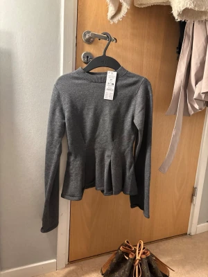 Grå peplumstickad tröja - Säljer en grå stickad tröja från Gina tricot med peplumdetalj i midjan och långa ärmar. Tröjan har rund halsringning och är tillverkad i mjukt stickat material, perfekt för lager på lager och en snygg vardagslook.🤍