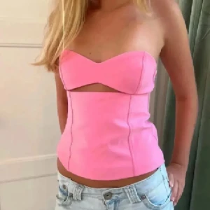 Rosa axelbandslös korsettopp - Snygg rosa korsettopp med axelbandslös design och markerade sömmar. Toppen har en cool cut-out detalj framtill och är perfekt att styla med jeans eller kjol. Trendig och figurnära passform som ger en modern look.