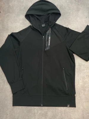 Nike tröja - Snygg svart hoodie med dragkedja framtill och två sidofickor med dragkedja. Huva med meshfoder och en extra bröstficka med dragkedja och Nike Running-tryck. Perfekt för dig som gillar sportig stil och funktionella detaljer.