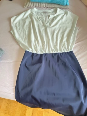 Vit och marinblå klänning från Esprit - Snygg tvåfärgad klänning från Esprit med vit överdel och marinblå kjoldel. Klänningen har korta ärmar, markerad midja och en avslappnad passform. Perfekt för dig som gillar enkel men stilren design.
