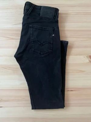 Svarta slim fit jeans från Replay - Säljer ett par svarta slim fit jeans från Replay med klassisk femficksdesign och diskreta sömmar. Jeansen har en snygg, smal passform och är tillverkade i stretchigt denimtyg för extra komfort. Perfekta för dig som gillar en stilren och modern look.