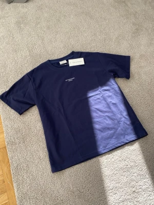 Marinblå t-shirt från Drôle de Monsieur - Snygg marinblå t-shirt från Drôle de Monsieur med vit text 'Not From Paris Madame' på bröstet. Klassisk rund hals och korta ärmar, perfekt för en avslappnad och cool look. Gjord i mjuk bomull som känns skön mot huden.