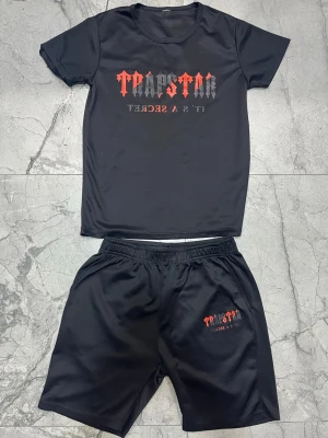 Svart set med tryck från Trapstar - Säljer Euro svart tvådelat set från Trapstar med t-shirt och shorts. Båda delarna har tryck i rött och grått med texten 'Trapstar It's a Secret'. Materialet är mjukt och stretchigt, troligen polyester. Perfekt för en avslappnad och trendig look.