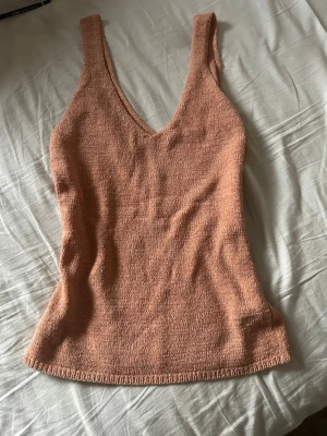 Beige linnetopp med v-ringning - Säljer en snygg beige linnetopp med djup v-ringning och breda axelband. Toppen har en enkel, stilren design och är tillverkad i ett mjukt, strukturerat material som känns skönt mot huden. Perfekt för varma dagar eller som layering-plagg.