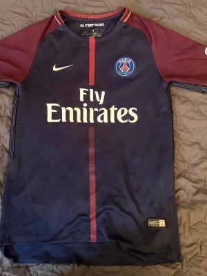 PSG Neymar Jr matchtröja Nike - Mörkblå och vinröd Paris Saint-Germain matchtröja med Neymar Jr och nummer 10 på ryggen. Tröjan har vita logotyper, Fly Emirates-tryck på bröstet och detaljer i rött. Tillverkad i lätt och ventilerande material. Passar folk som är ca 155 med storleken 158. 