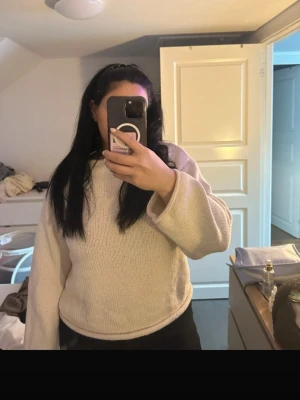 Beige stickad tröja med vida ärmar - Säljer en enkel och stilren beige stickad tröja med rund hals och vida ärmar. Tröjan är mjuk och har en avslappnad passform, perfekt att slänga på sig när det är kyligt. Materialet ser ut att vara bomull eller en bomullsblandning.