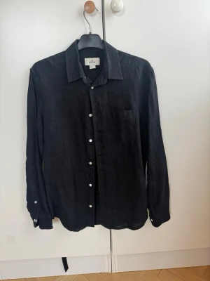 Svart linneskjorta från h&m edition  - Stilren svart linnekjorta från hm i luftigt linne. Klassisk krage, vita knappar framtill och i fint skick. Nypris 699 kr 