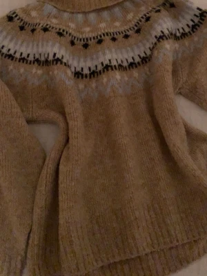 H&M Brun turtleneck i srlk M - Stickad tröja i beige med rund hals och klassiskt nordiskt mönster i svart och vitt runt oket. 