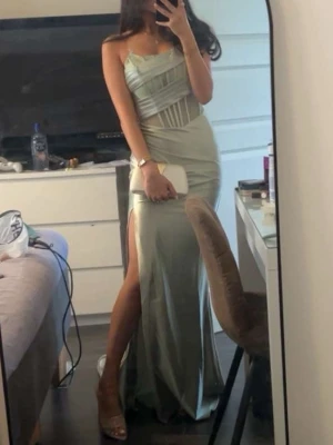 Ljusgrön axelbandslös maxiklänning - Ljusgrön lång klänning med slits som är lagom hög. Korsett överdel med inbyggda pads för support. Går även att lägga till BH-band för extra support men funkar perfekt utan också. Använd en gång. Jättefin inför bal, bröllop eller andra fester. 