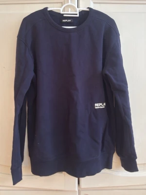 Mörkblå sweatshirt från Replay - Mörkblå sweatshirt från Replay med rund halsringning och tryckt vit logga samt textdetalj på framsidan. Tröjan har långa ärmar och ribbade muddar vid ärmslut och nederkant. Perfekt för en avslappnad och stilren look.
