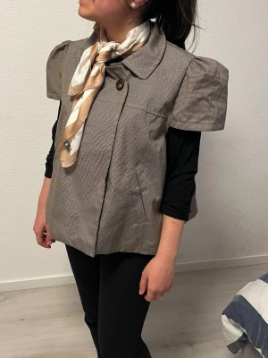 Rutig overshirt med puffärm - Snygg rutig overshirt i beige och brunt med bred krage och puffiga korta ärmar. Jackan har knappar framtill och fickor på sidorna. Tillverkad i ett mjukt bomullsmaterial och har en loose passform som ger en avslappnad vibe.