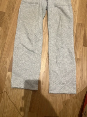 Grå mjukisbyxor med raka ben - Säljer ett par ljusgrå mjukisbyxor med raka ben och resår i midjan. Byxorna har två fickor fram och är gjorda i mjukt sweatshirtmaterial, perfekta för chill dagar. Passar dig som gillar enkel och clean stil.