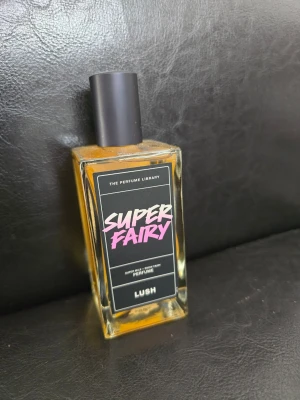 Lush Super Fairy parfym 100ml - Super Fairy från Lush är en parfym i en snygg, rektangulär glasflaska med svart etikett och färgglad text. Perfekt för dig som gillar unika och lekfulla dofter. Provad men är så gott som nästan full.