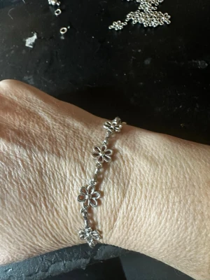 Silverfärgat armband med blommor - Ett stilrent armband i silverfärg med flera små blommor som länkar. Blommorna har en öppen design och armbandet har ett smidigt magnetlås. Perfekt för dig som gillar detaljerade och lekfulla smycken i metall.